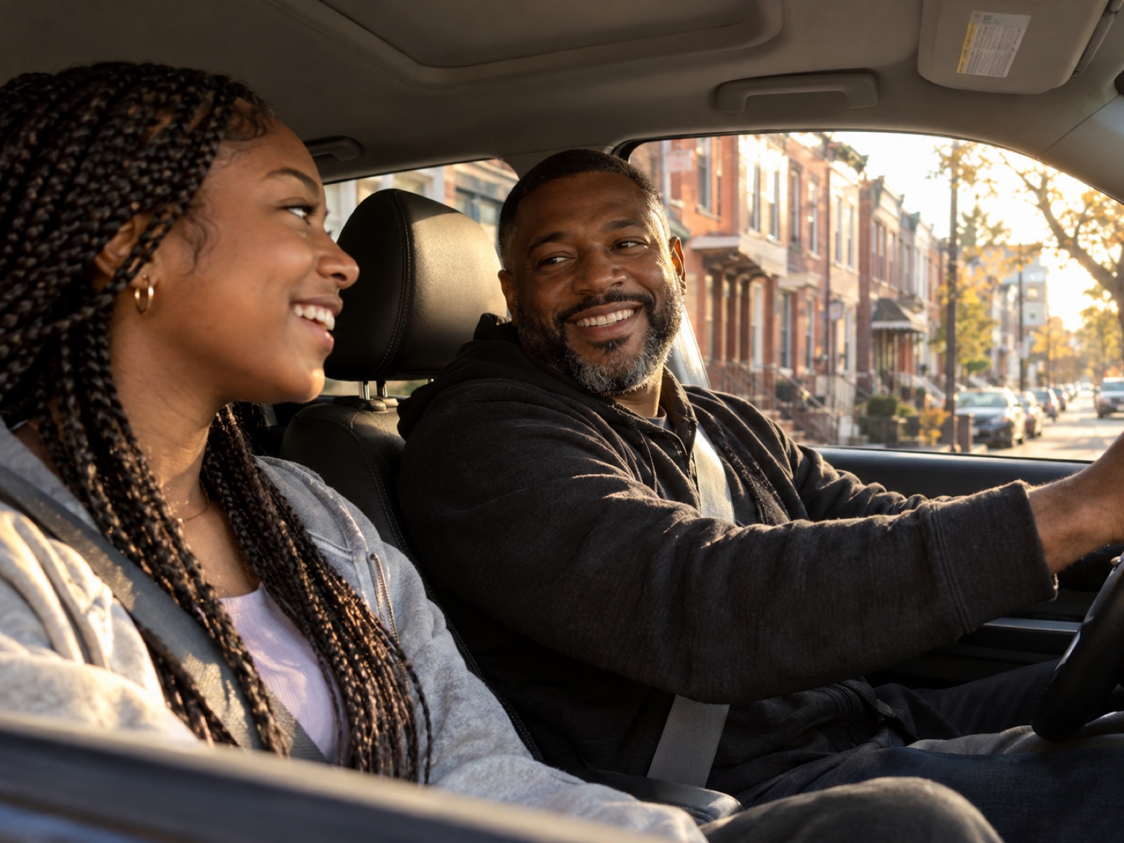 A Black father driving and laughing with his teenage daughter on a Philadelphia street